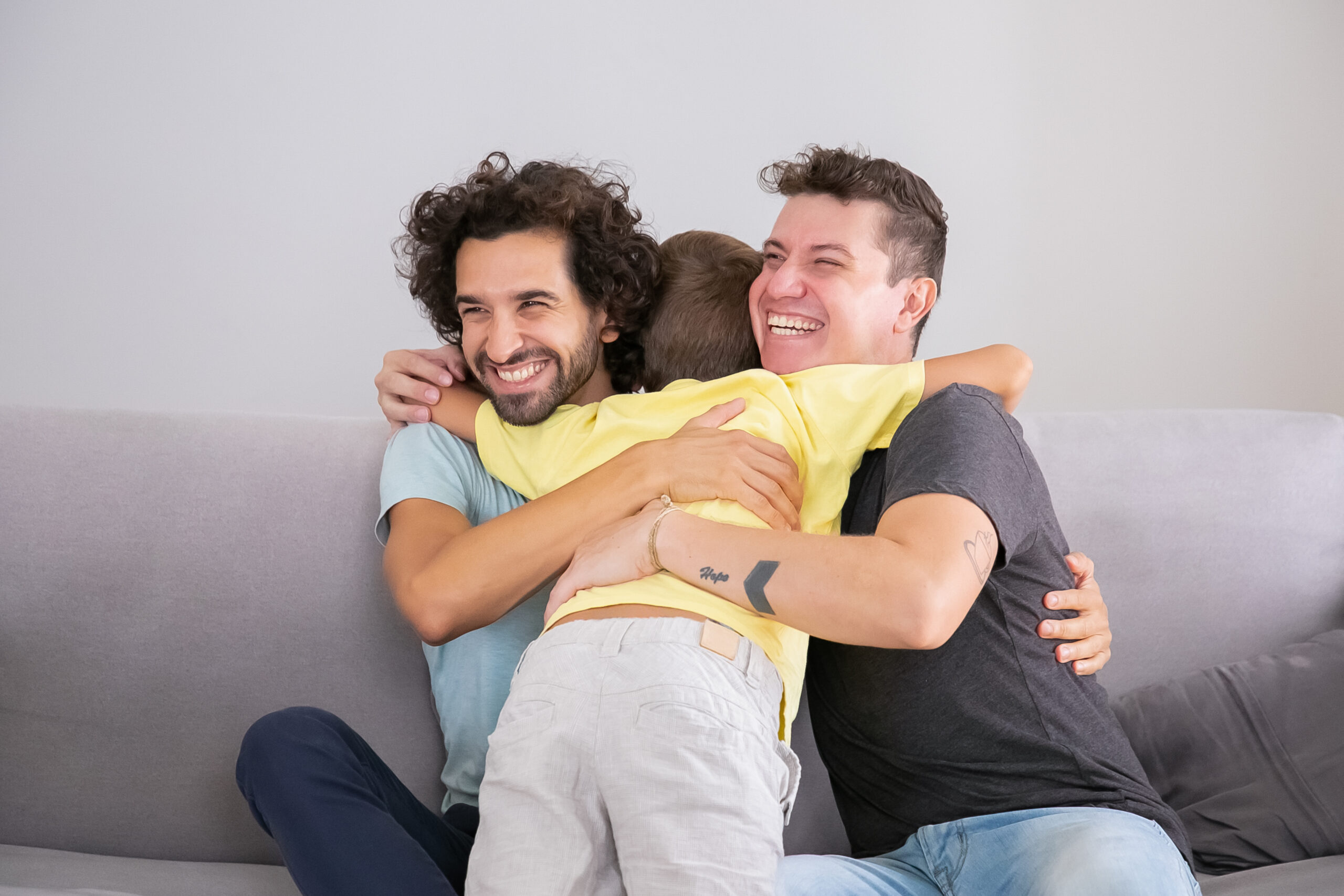 Little son hugging two happy handsome fathers at home. Medium shot. Happy family and parenthood concept